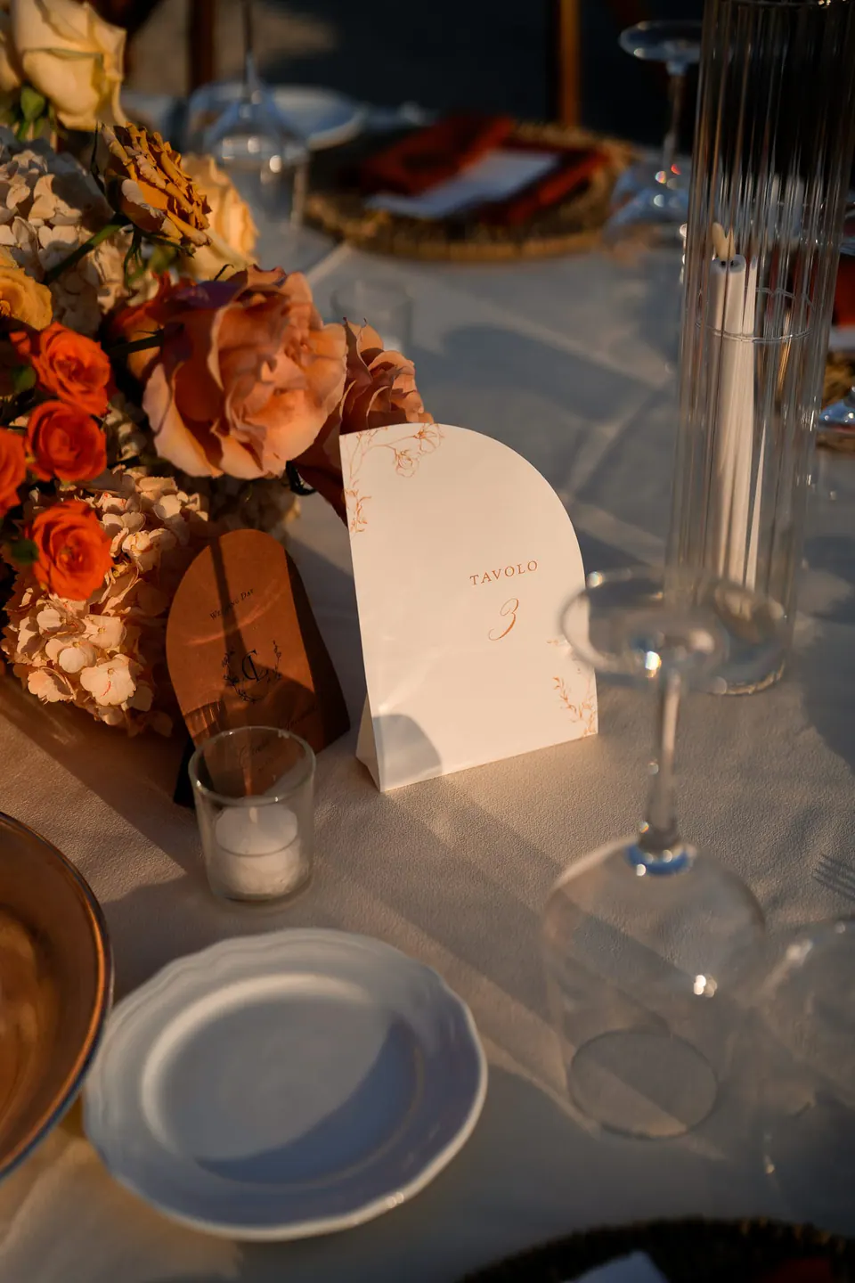 Platzkarte und Gläser auf dem Dinnertisch, orange Blumen in Unschärfe.