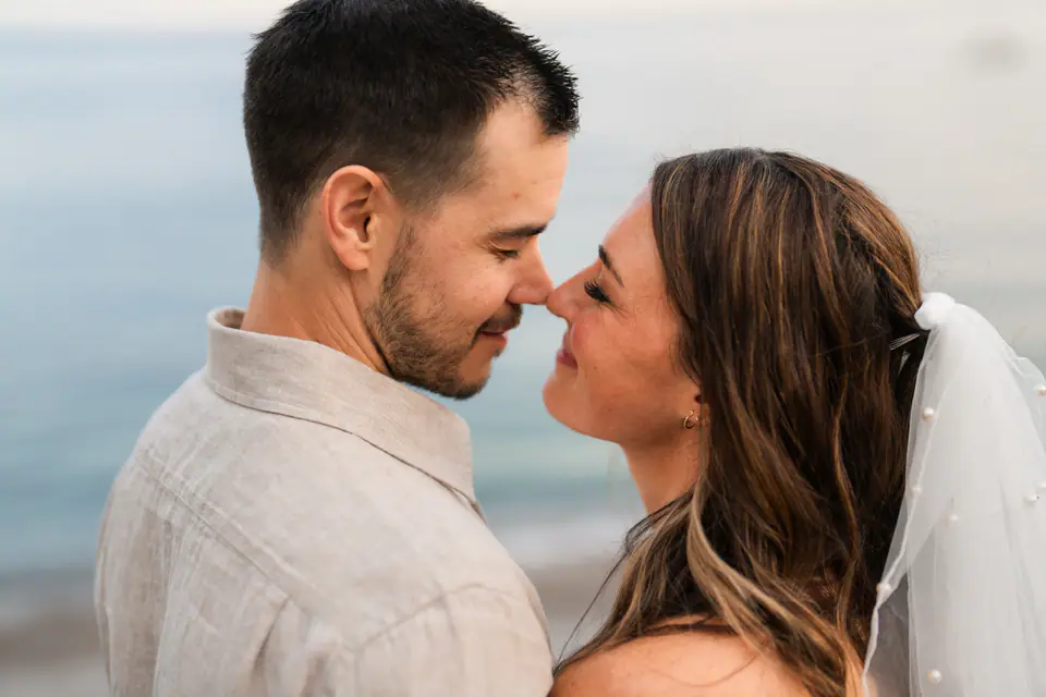 The couple nose to nose against the soft blue of the sea.