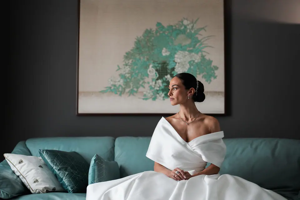 Sposa seduta su un divano turchese sotto un dipinto.