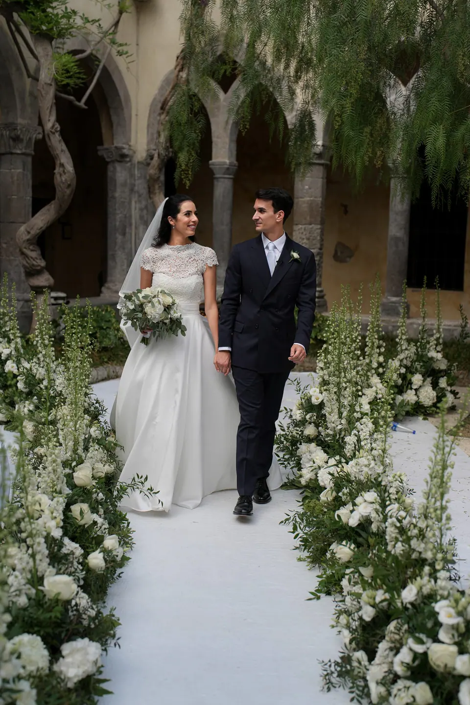 Bride and groom walking down the flower-lined aisle of the cloister after the ceremony