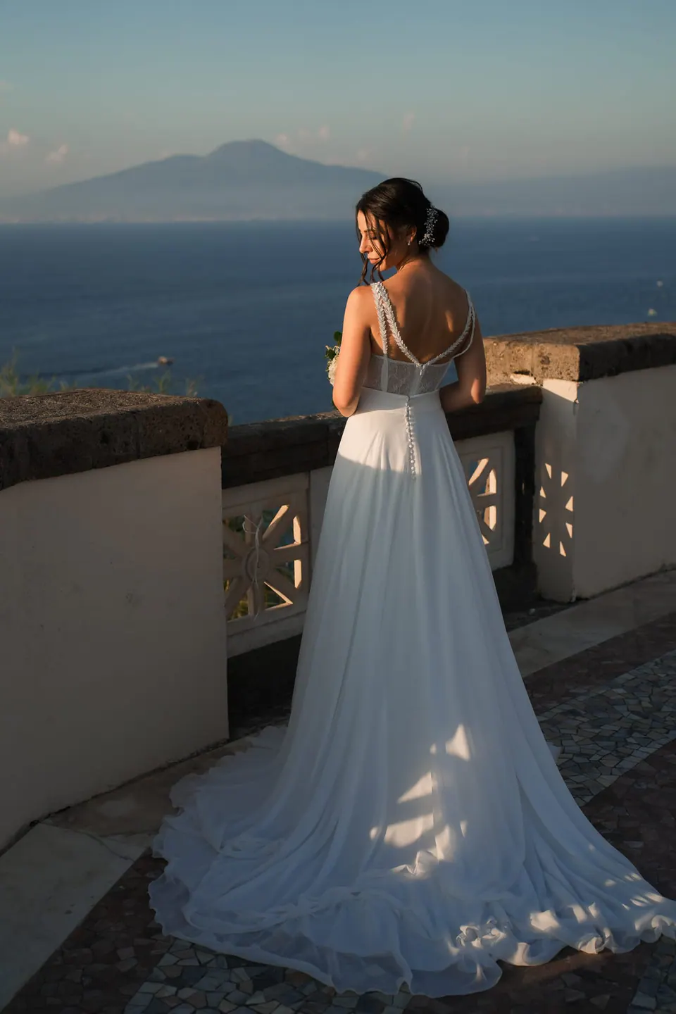 Bride seen from behind on the villa terrace, Vesuvius across the gulf in the evening light.