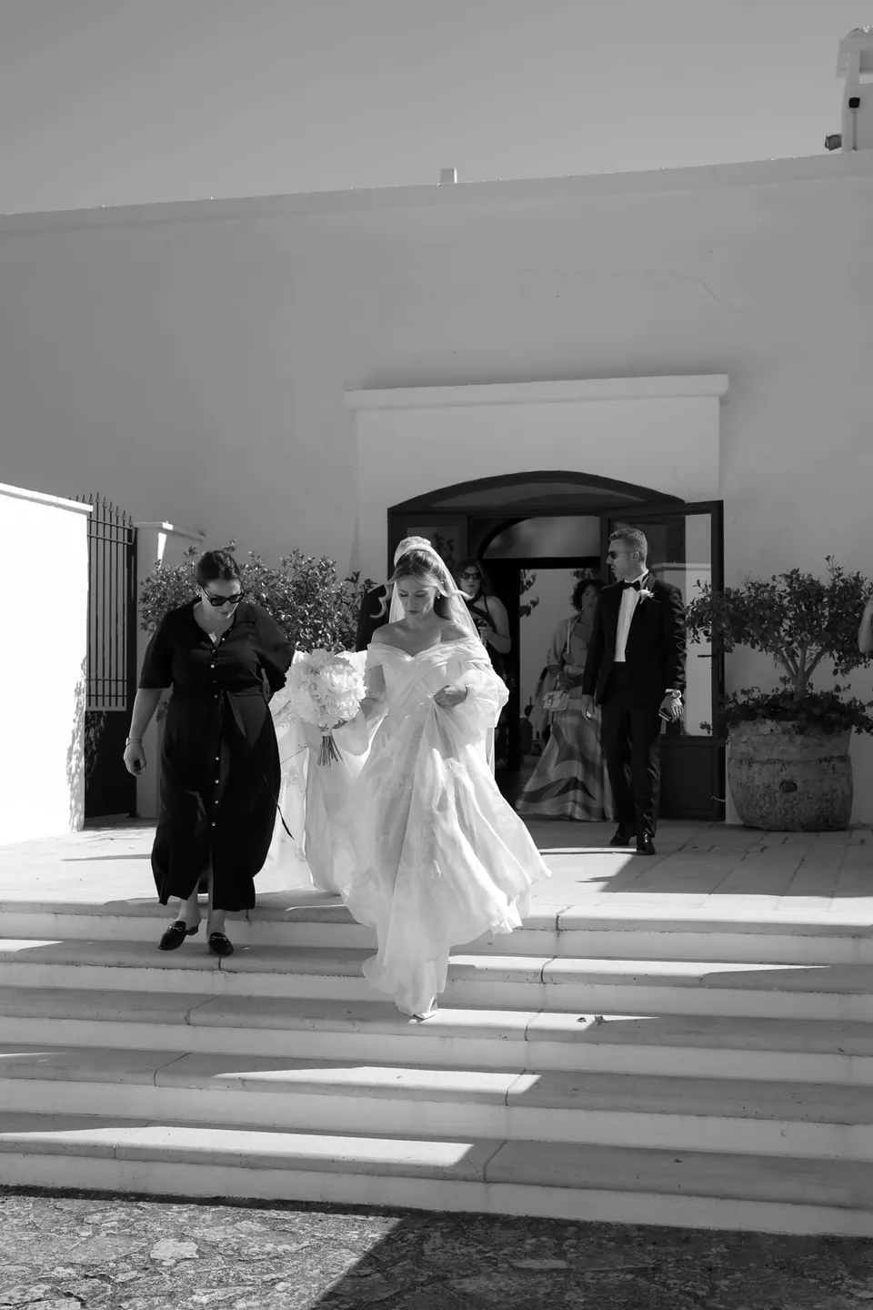 Foto en blanco y negro de la novia bajando los escalones con dos invitados.