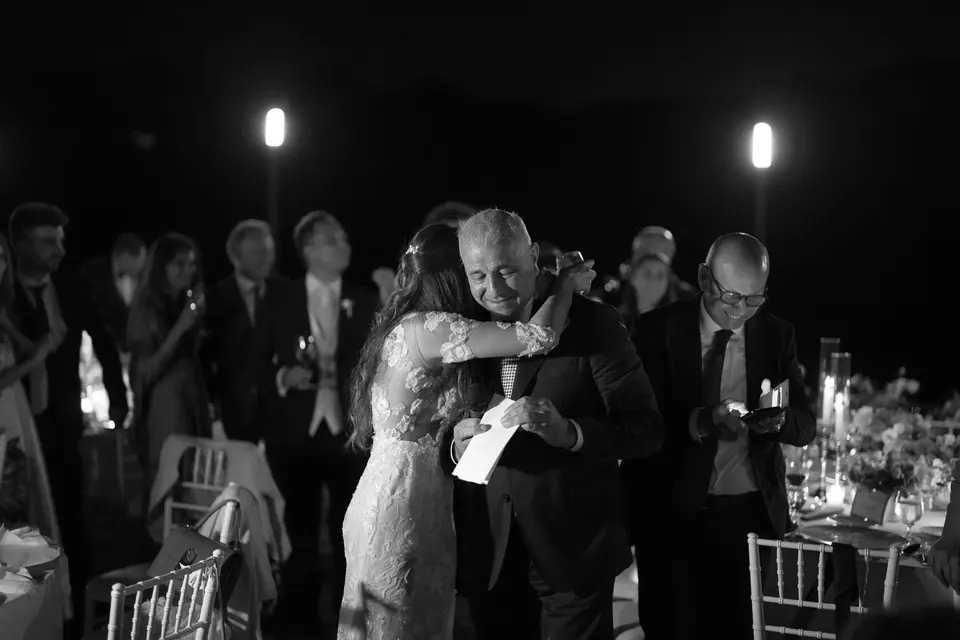 Schwarzweißfoto: Die Braut umarmt beim Dinner einen älteren Gast.