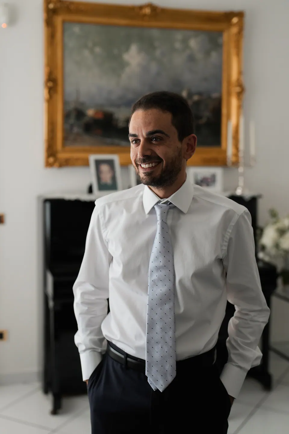 Groom in shirt and tie beneath a gilt-framed painting before the ceremony.