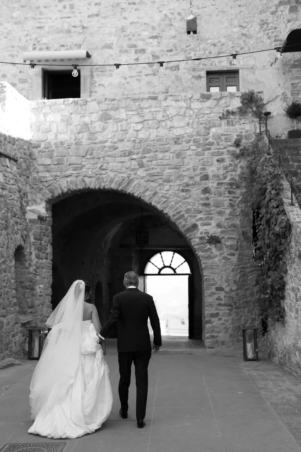 Foto in bianco e nero degli sposi che camminano verso la porta ad arco del castello.