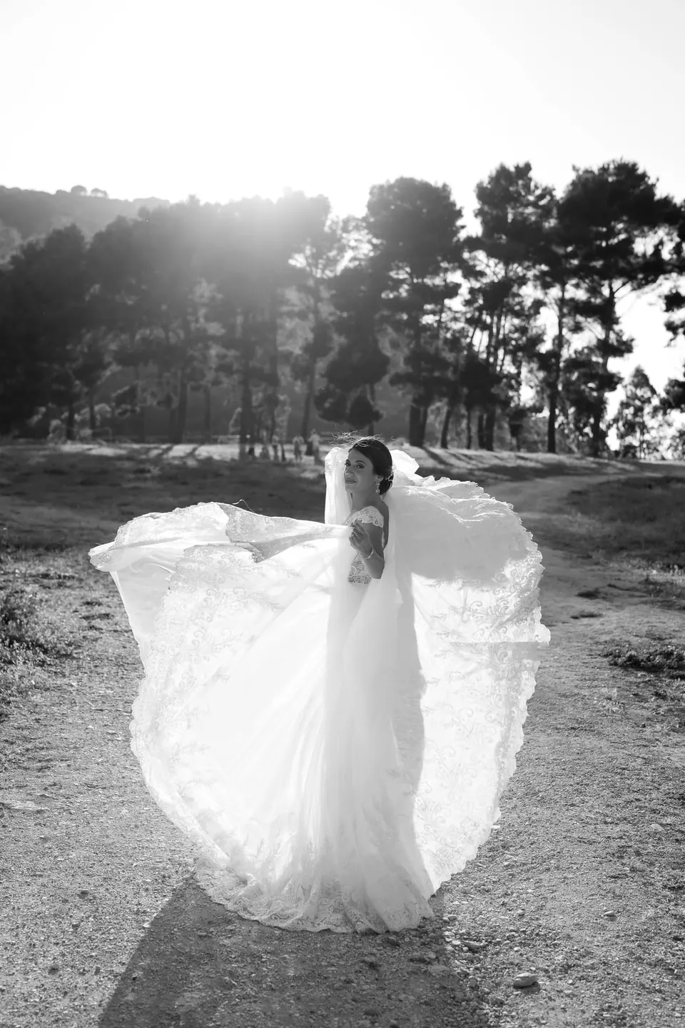 Black and white photo of the bride spreading her dress in a pine grove