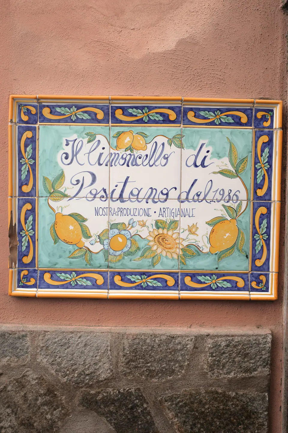 Hand-painted ceramic sign of Positano on a pink wall.