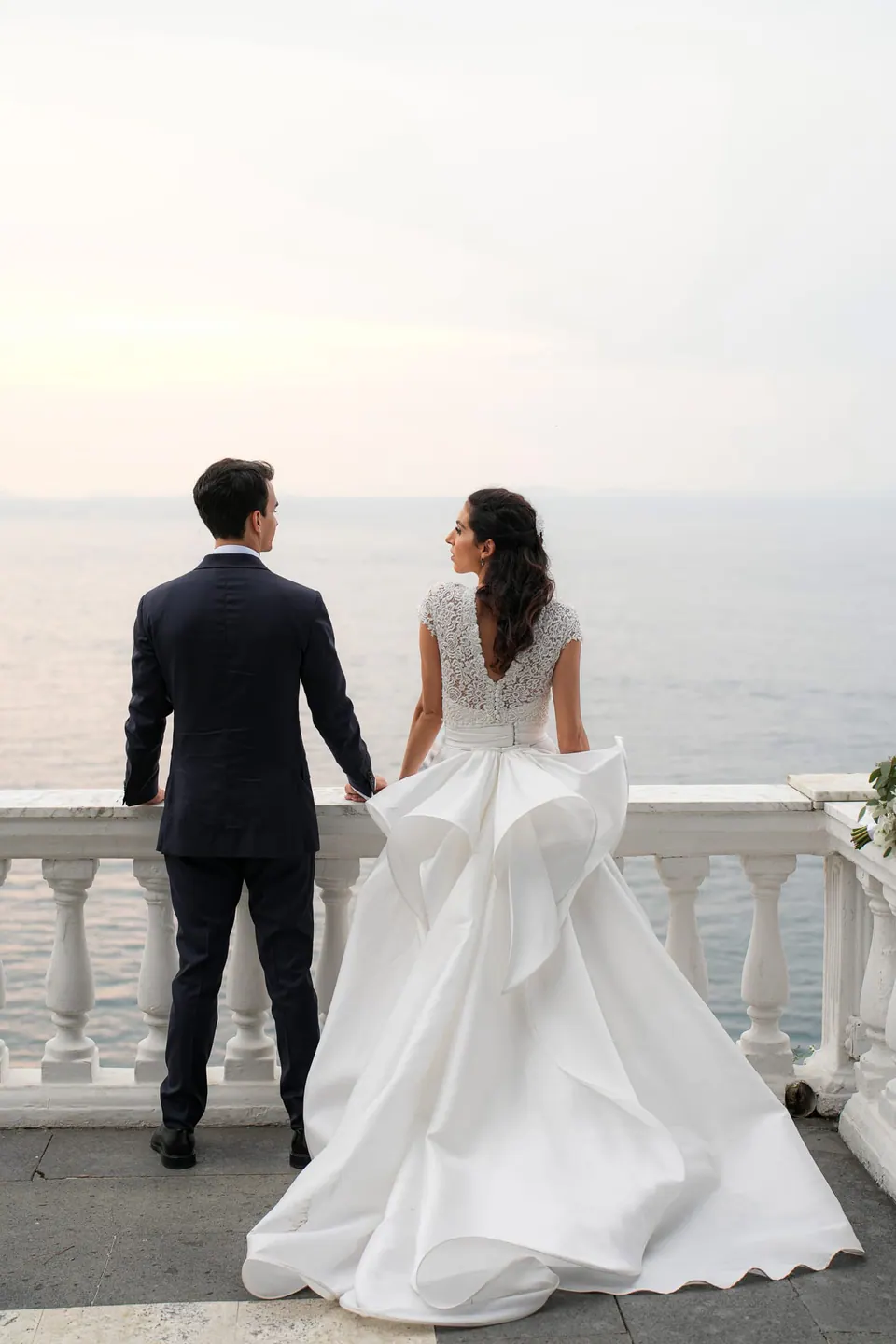 Bride and groom seen from behind at the terrace balustrade above the sea