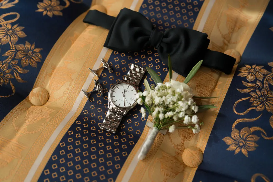 Groom's tie, cufflinks and buttonhole flower on a gold patterned surface.