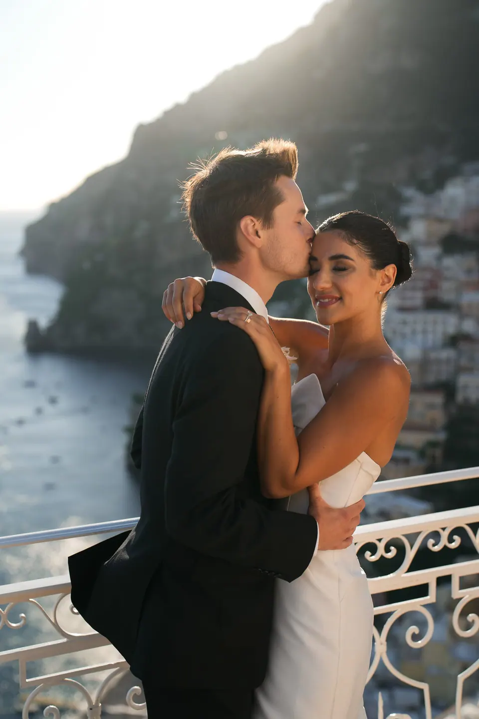 Groom kissing the bride's forehead at the railing.