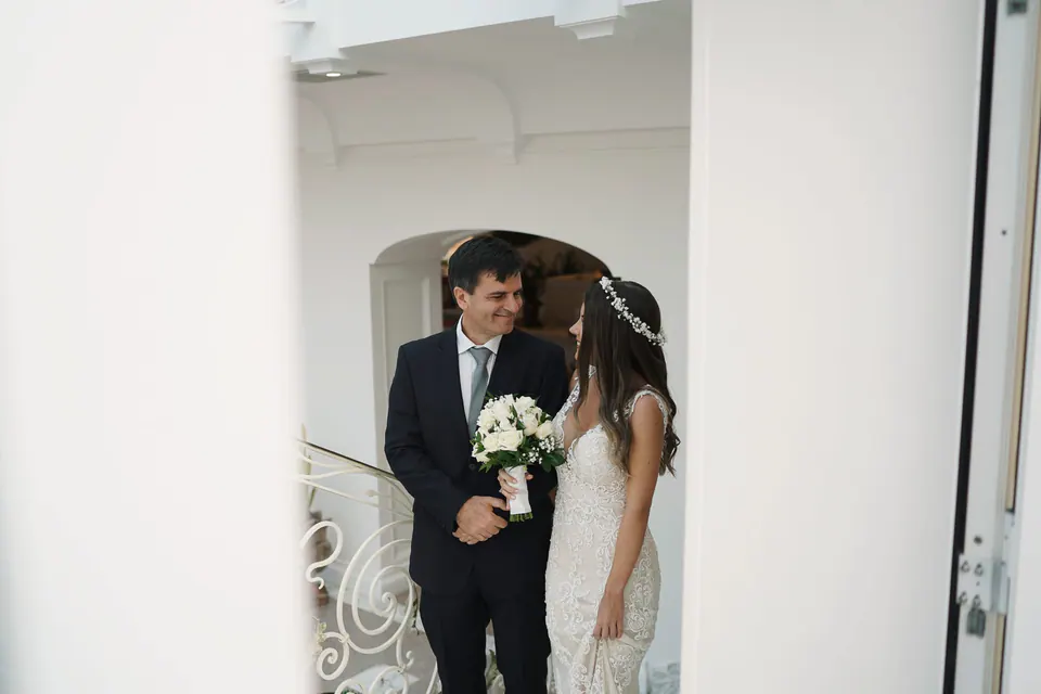 Bride and groom in a white doorway of Hotel Corallo, bouquet in hand.