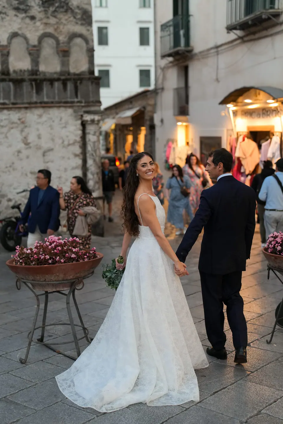 Bride and groom holding hands in the piazza of Amalfi in the evening.