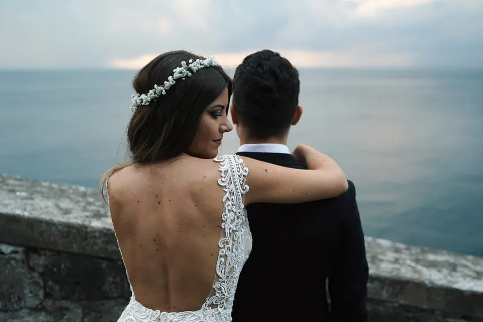 Bride and groom from behind, intimate embrace with soft light and sea in the background.