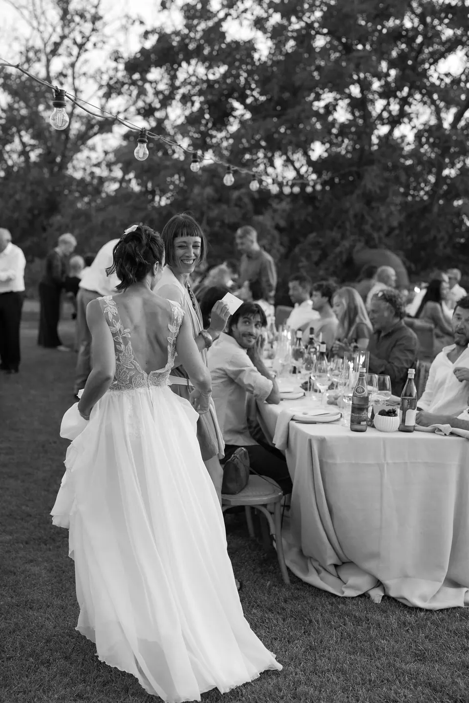 Black and white photo of the bride seen from behind among the dinner tables