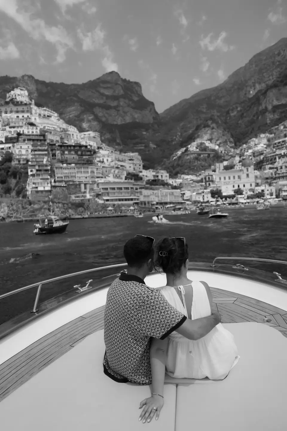 Black and white photo of the couple from behind on the bow, Positano ahead.