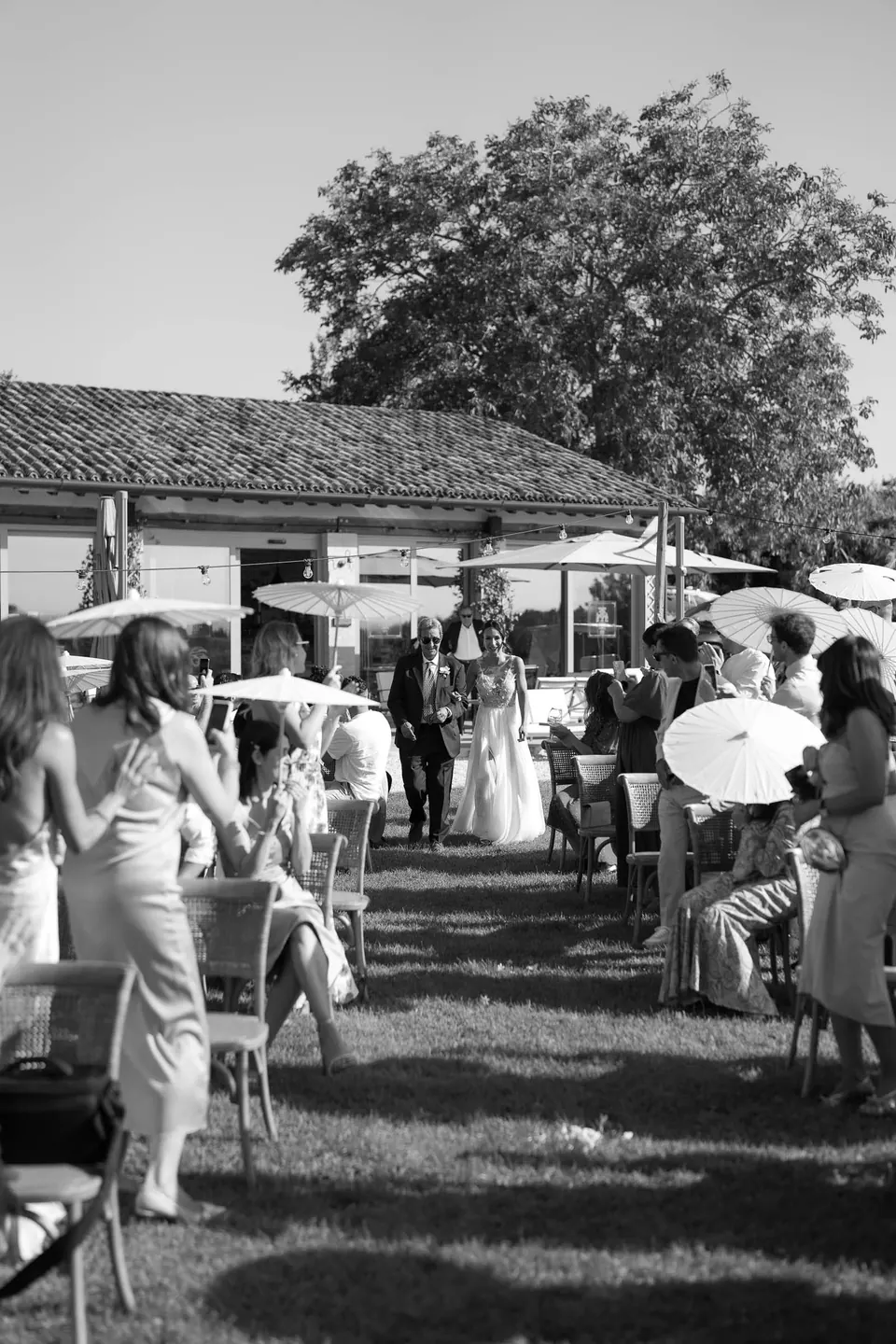 Black and white photo of guests seated with parasols at the ceremony