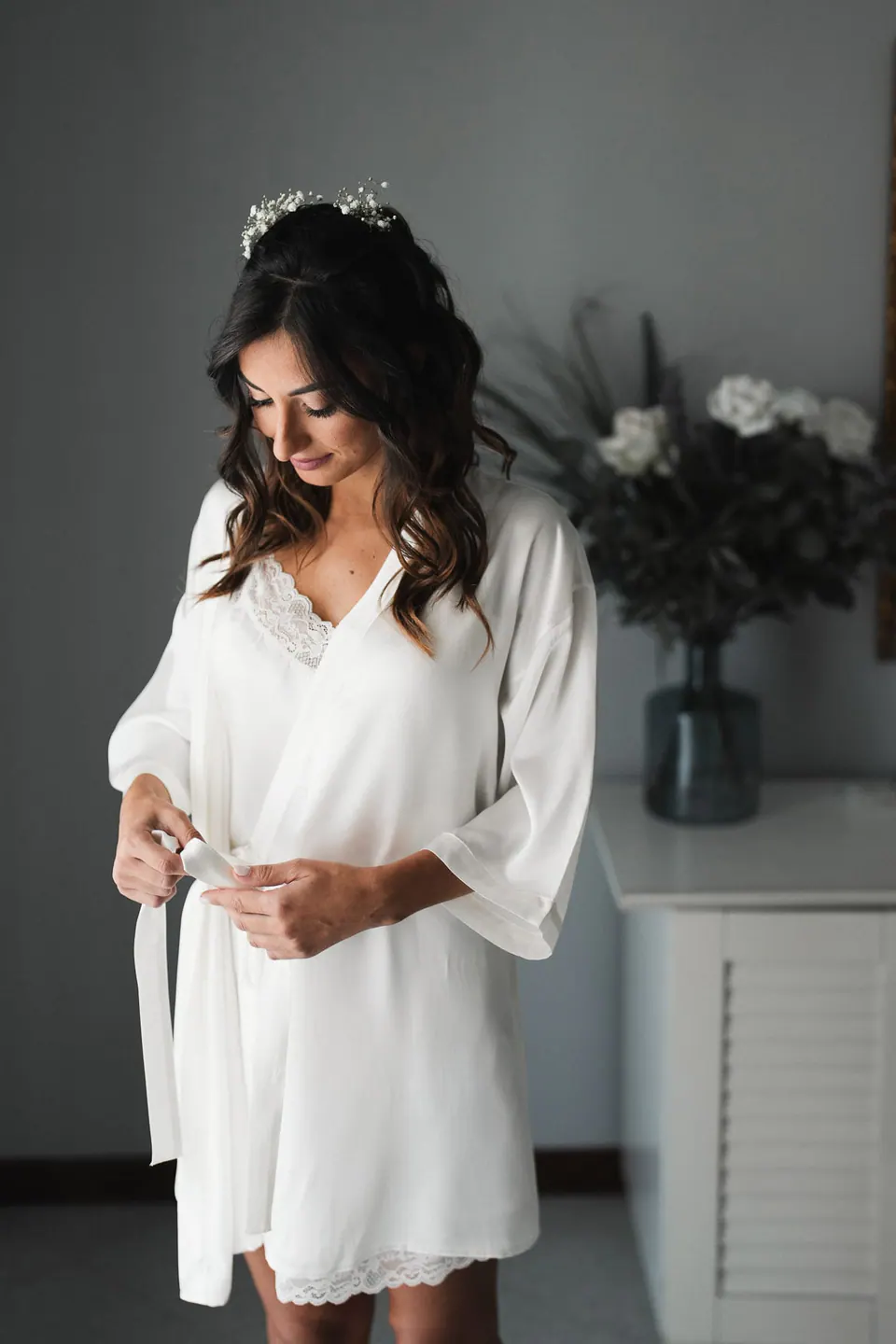 La sposa sorride con un abito di seta prima di indossare l'abito, mentre una luce soffusa riempie la sala della villa.