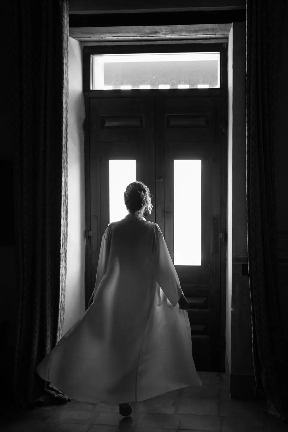Sagoma in bianco e nero della sposa in un'alta porta, la luce alle spalle.