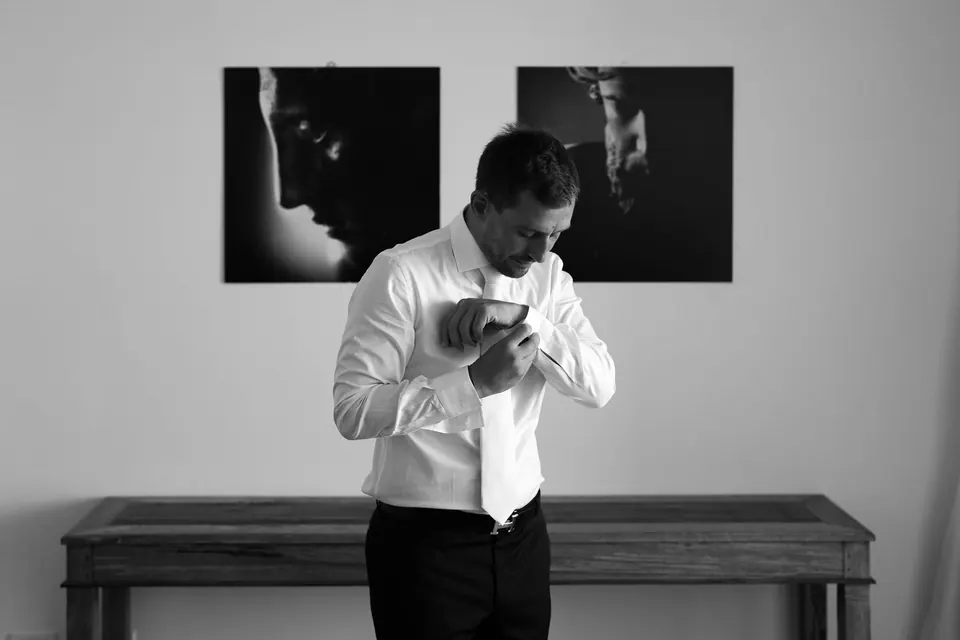 Lo sposo si abbottona la camicia in un interno moderno, composizione minimalista.