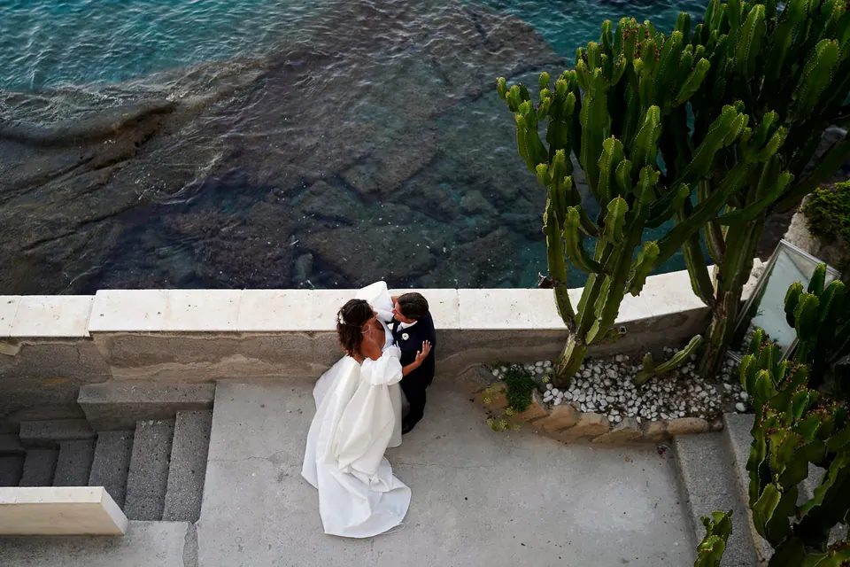 View from above of the couple on the seaside terrace, turquoise water and cacti around them.