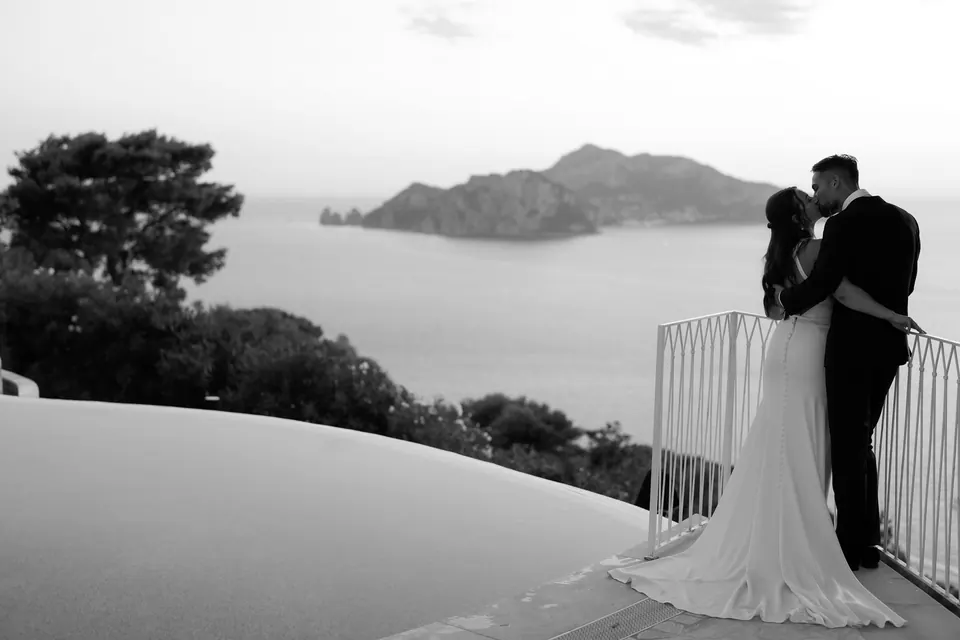 Black and white photo of the couple on the terrace with Capri in the distance.