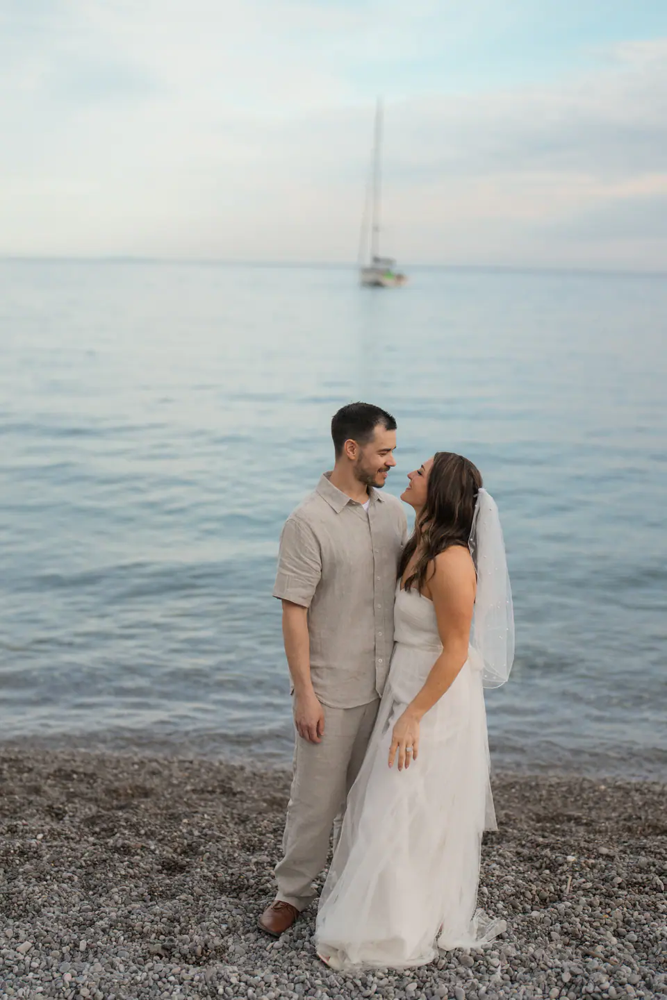 Couple embracing at the water's edge, a sailing boat in the bay.