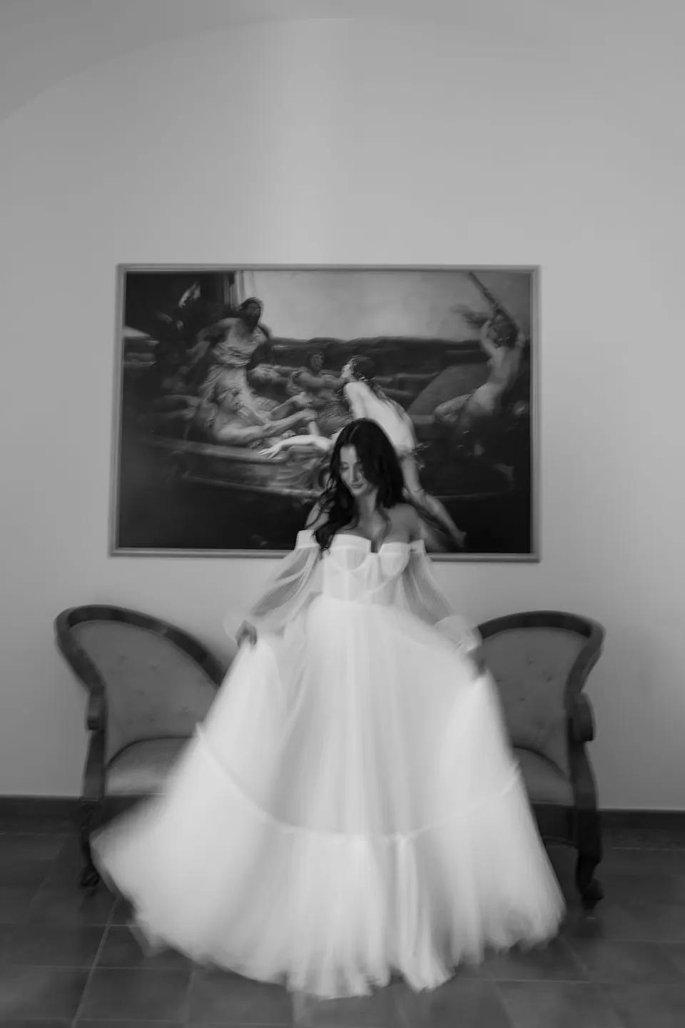 Schwarzweißporträt der Braut im Tüllkleid, sitzend unter einem alten Gemälde in der Villa.