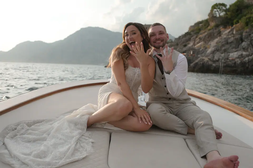 Couple laughing on the bow of the boat, the bride showing her ring.