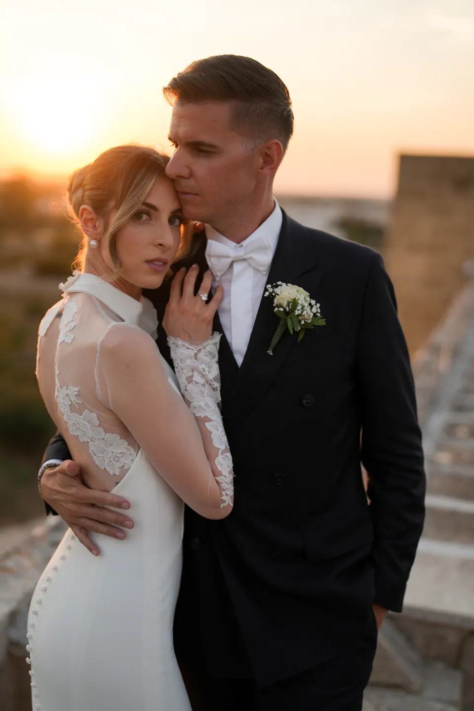 La sposa con la testa sul petto dello sposo e il tramonto salentino alle spalle.