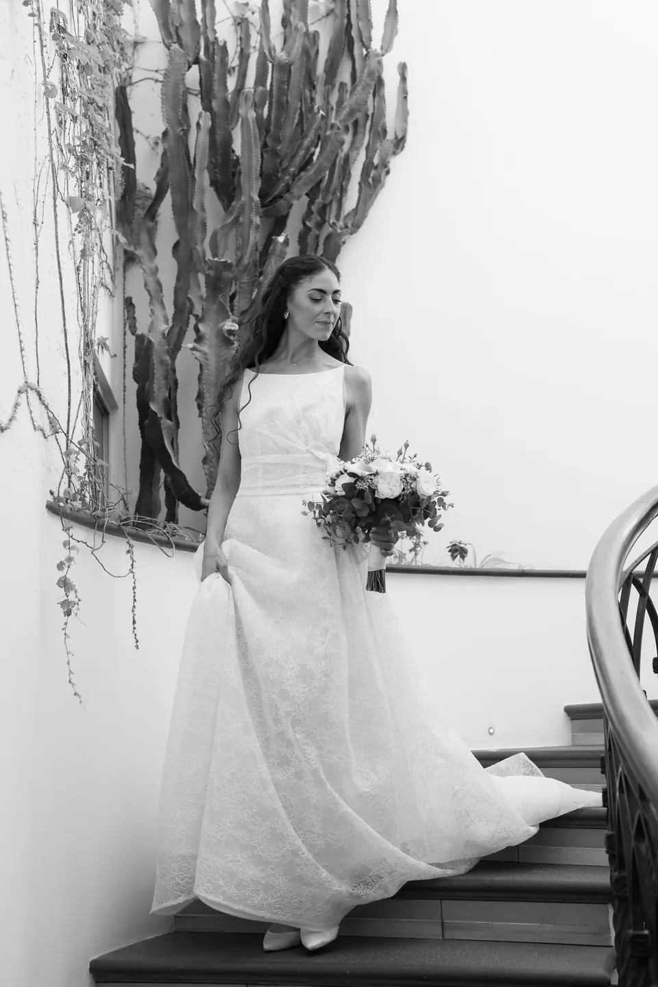 Black and white photo of the bride coming down the staircase beside a cactus.