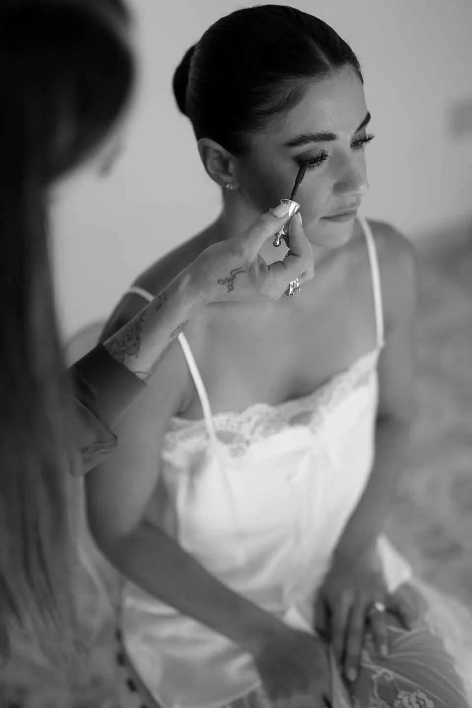 Black and white photo of the makeup artist applying mascara to the bride.