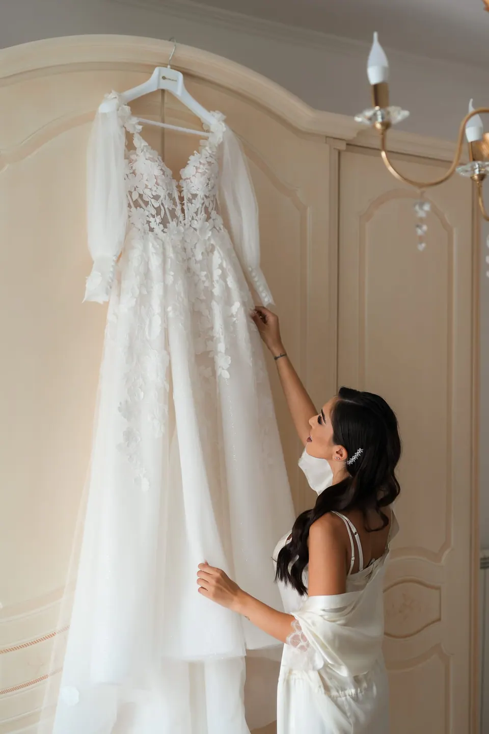 Bride in her robe reaching for the wedding gown hanging on the wardrobe.