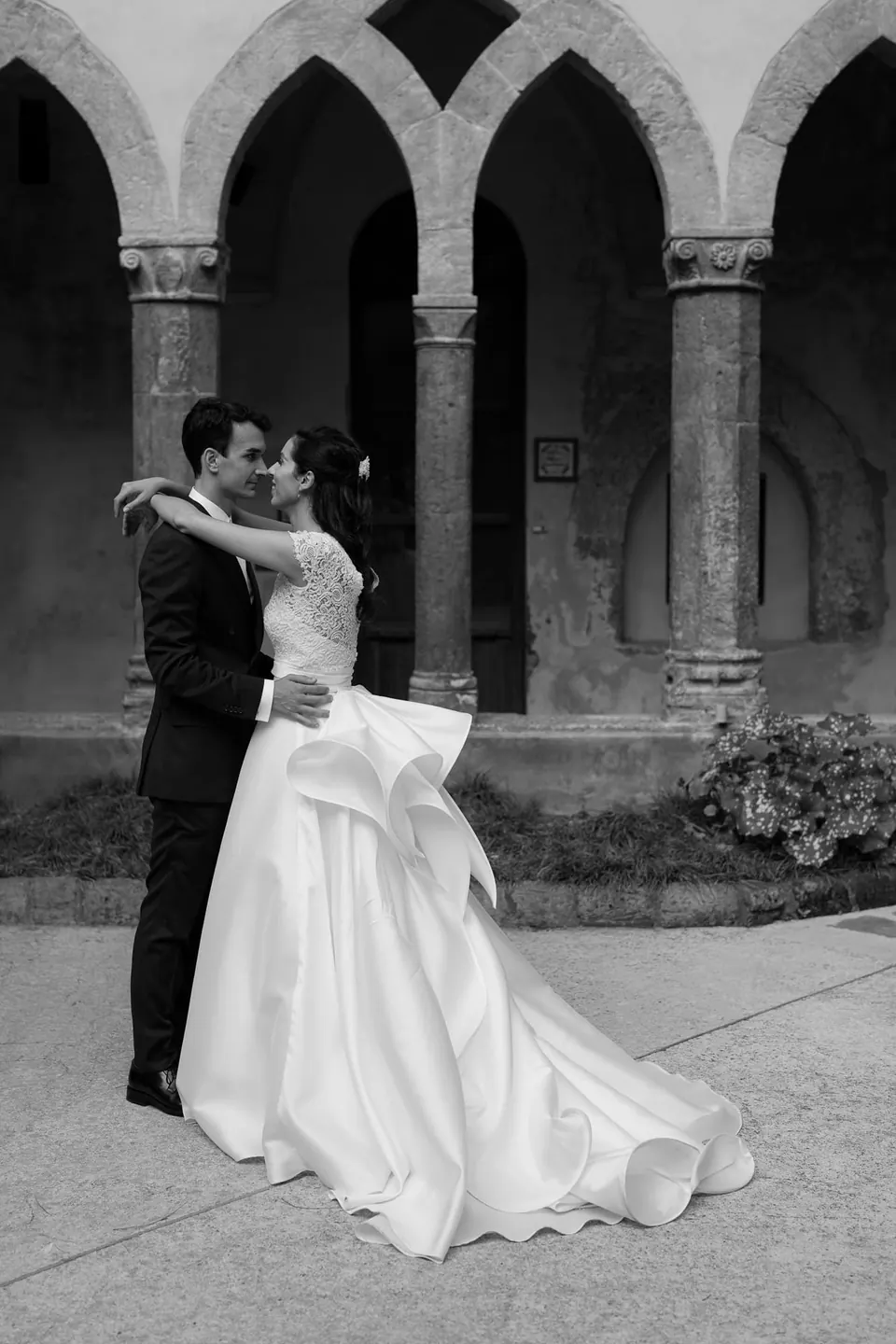Black and white photo of bride and groom embracing under the arches of the Chiostro di San Francesco, Sorrento