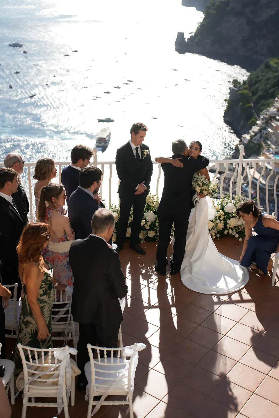 Ceremony on the terrace seen from behind the guests, the sea and cliffs ahead.