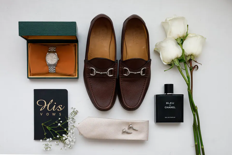 Les détails du marié : une montre vintage, des mocassins à mors, des roses blanches, un parfum et son carnet de vœux.