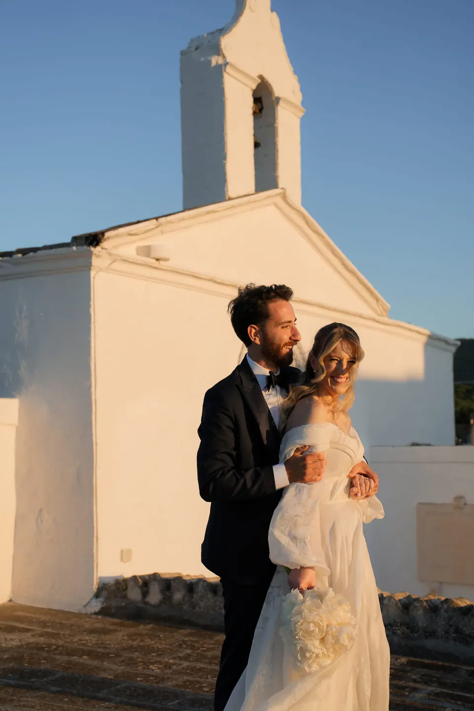 La pareja de la mano junto a una capilla blanca, boda en Italia.