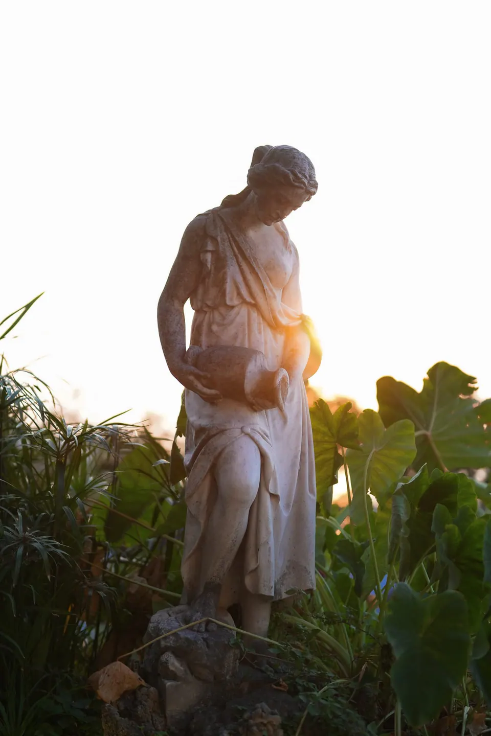 Eine Gartenstatue bei Sonnenuntergang zwischen Pflanzen.