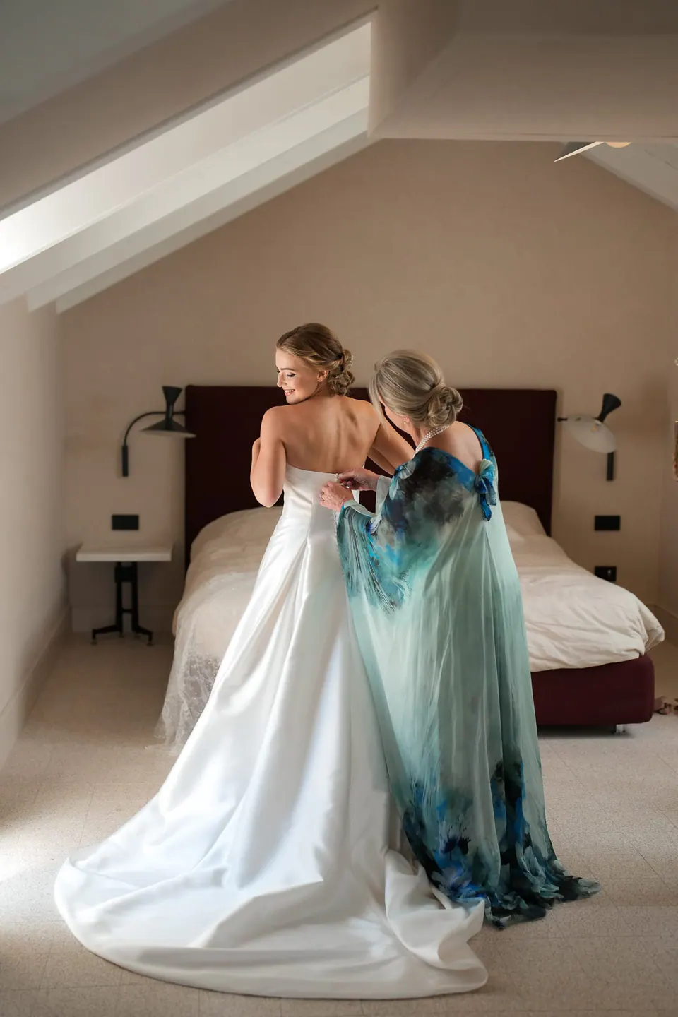 Die Mutter im blau-grün gemusterten Kleid hilft der Braut im Dachzimmer.