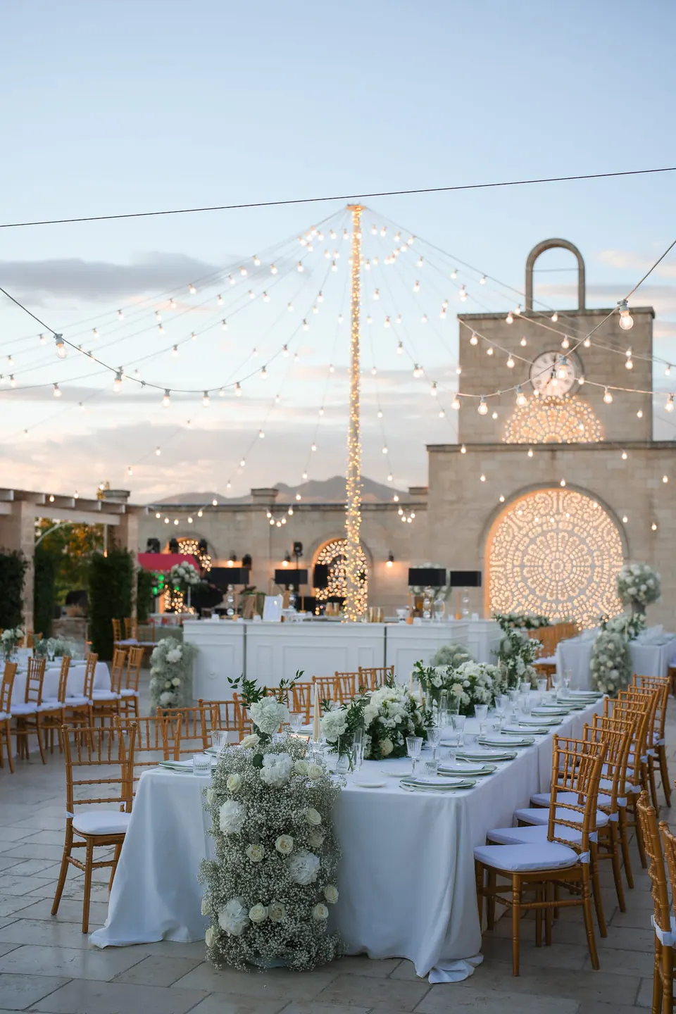 The courtyard set for dinner under the lights at dusk, the clock tower behind