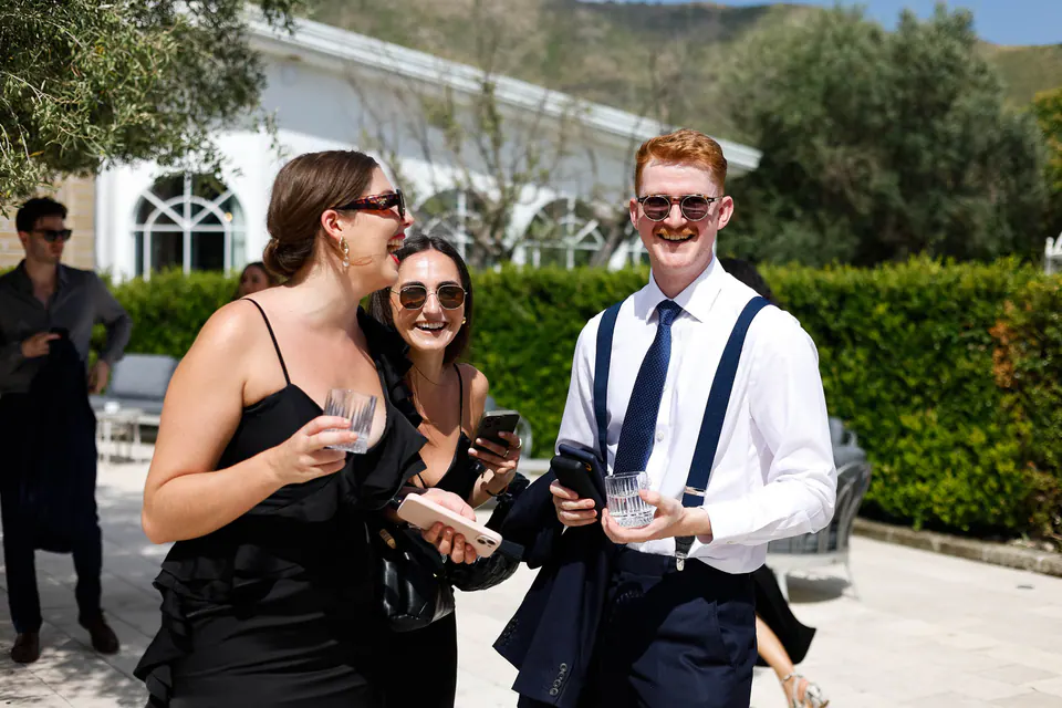 Des invités en lunettes de soleil rient ensemble sur la terrasse avant la cérémonie.