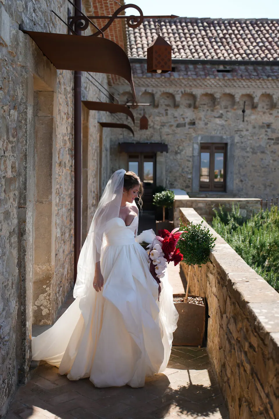 Sposa lungo il balcone in pietra, il velo che fluttua dietro.