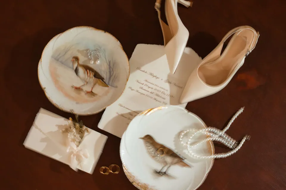 Zapatos de novia, alianzas e invitación sobre platos de porcelana con pájaros.