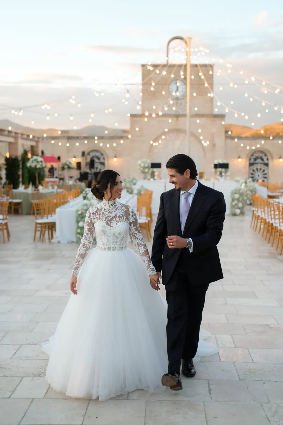 Bride and groom walking hand in hand after the ceremony, between flower arrangements.