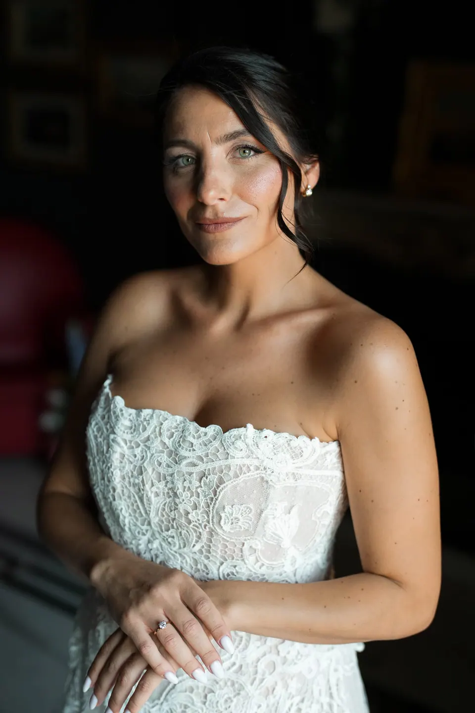 Porträt der Braut im trägerlosen Spitzenkleid vor einer dunklen Wand.
