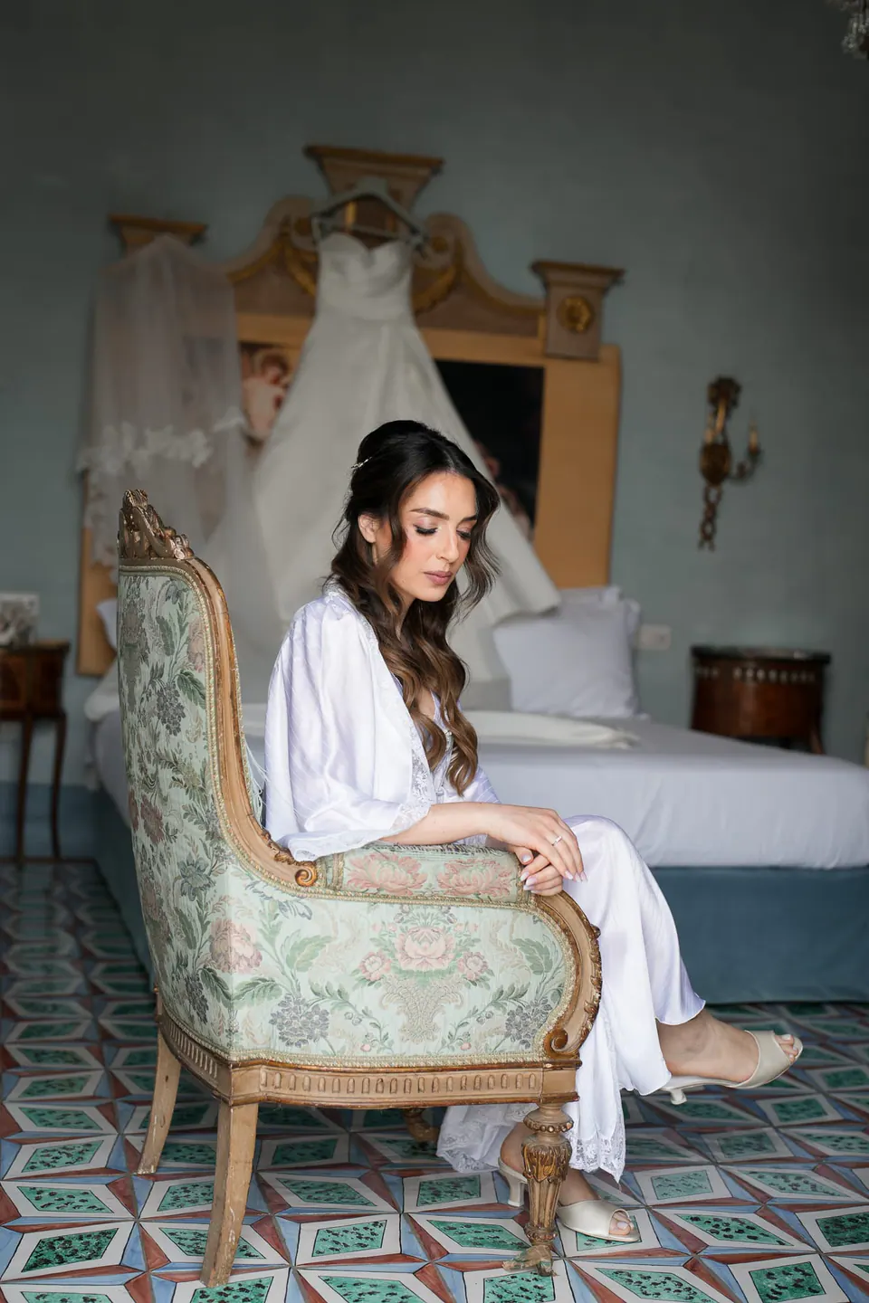 La novia en bata sentada en un sillón, con el vestido colgado detrás.