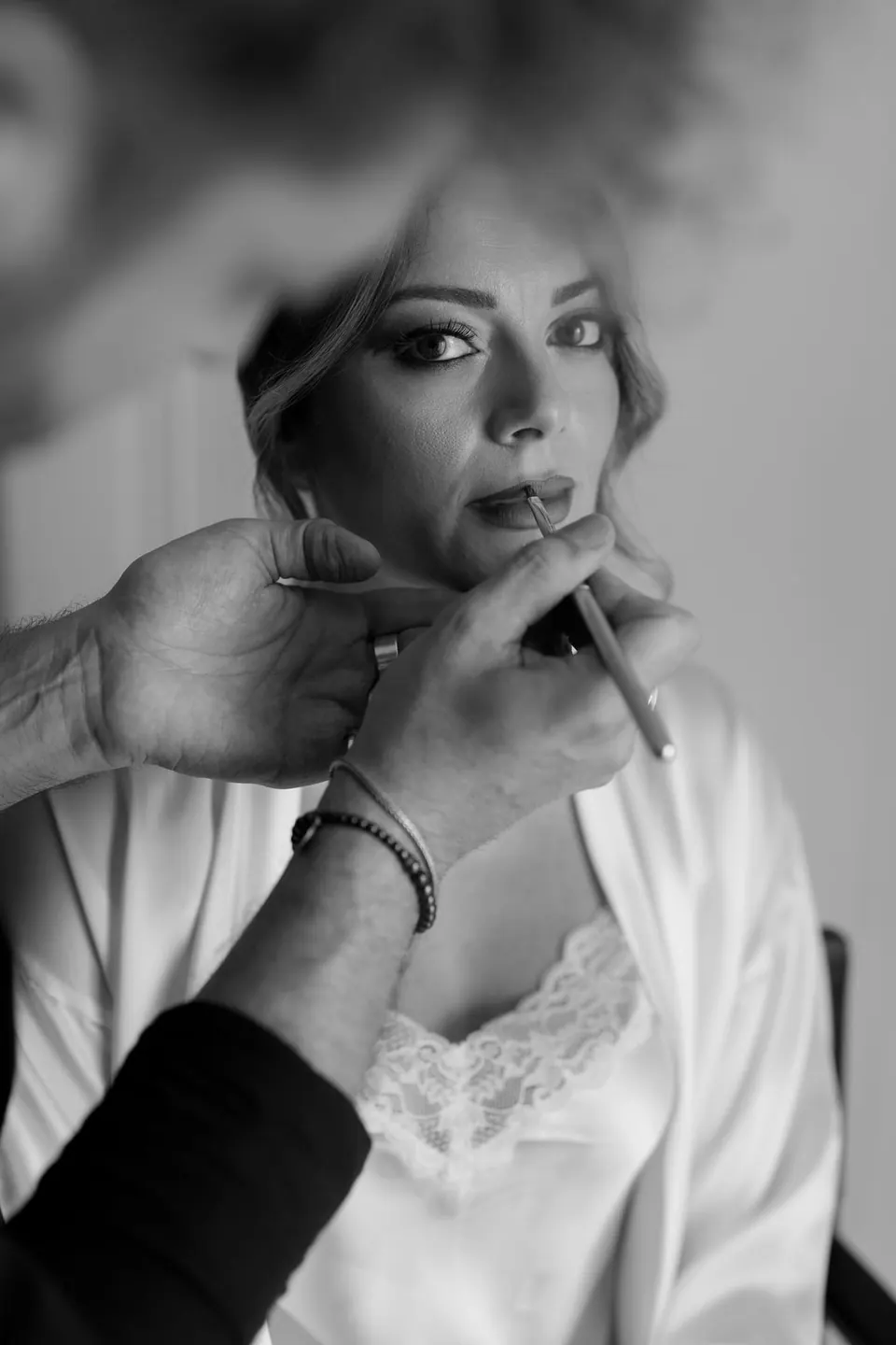 Bride applying lipstick while getting ready, soft natural light creating a serene mood.