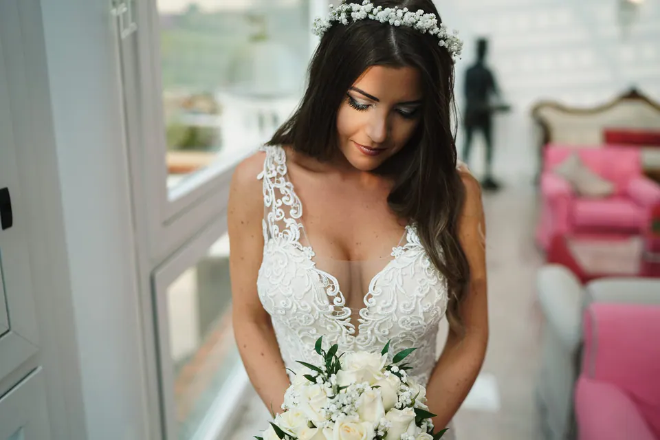 Bride holding her bouquet by a window in soft light.