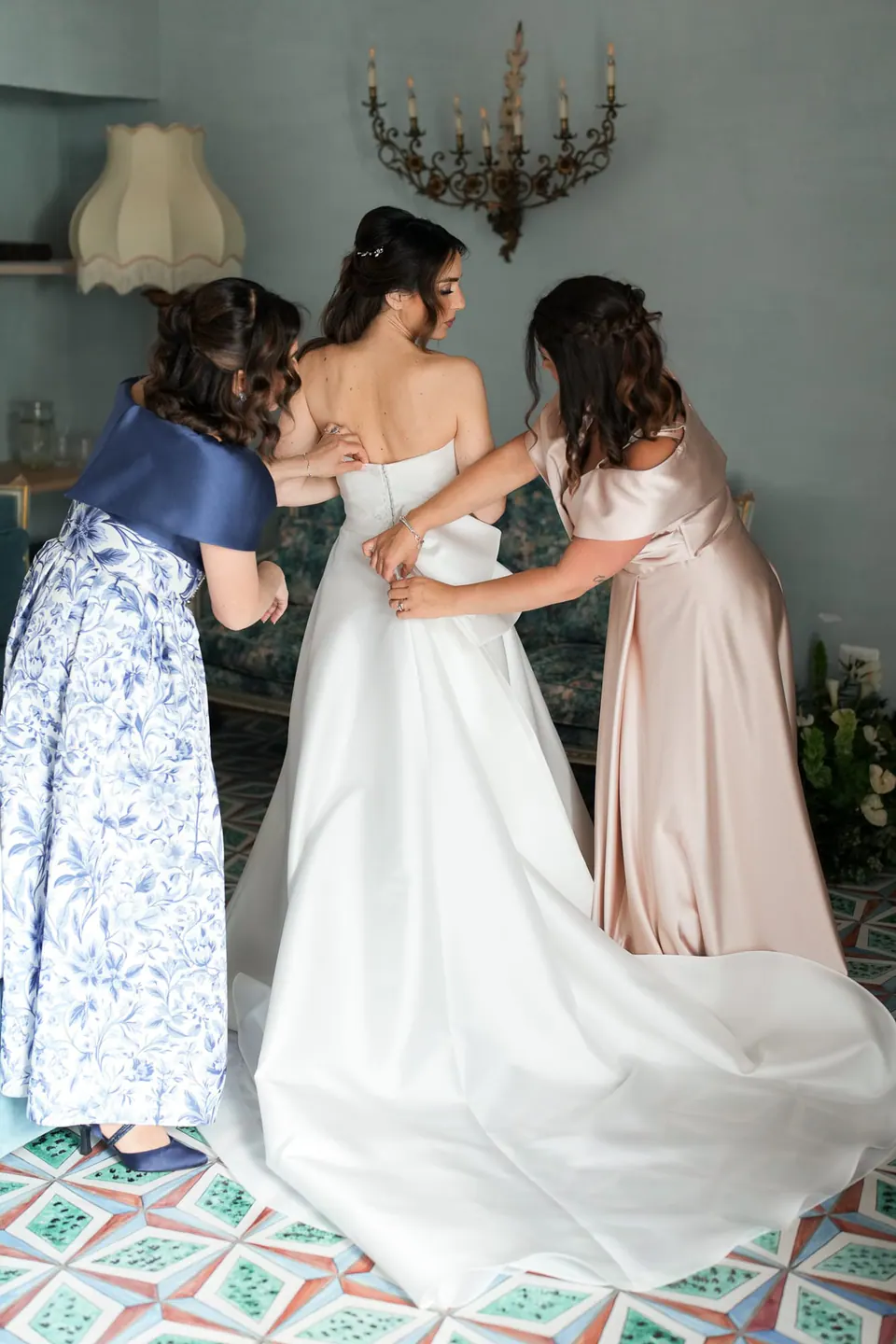 Unas mujeres abrochan el vestido de la novia en el dormitorio.