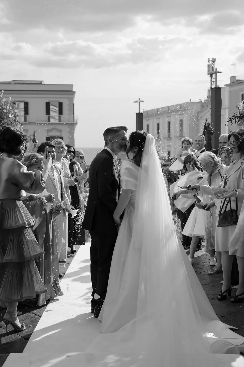 Foto en blanco y negro de los novios rodeados de invitados en la calle.