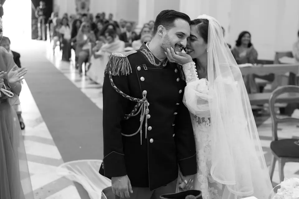 Black and white photo of the newlyweds walking back up the aisle, the groom in dress uniform.